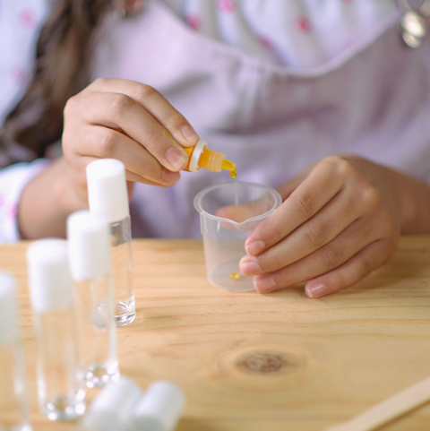 Person pouring a yellow liquid from a small bottle into a clear container on a wooden table.