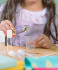 Child pouring a liquid from a bottle into a small container on a table.