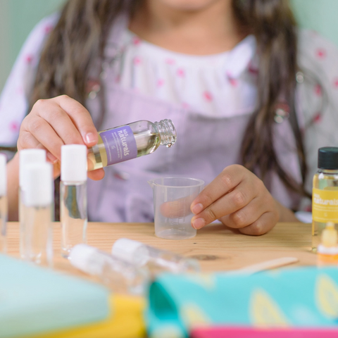 Child pouring a liquid from a bottle into a small container on a table.