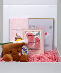 Valentine's Day gift box with plush toy, eye masks, and greeting card on a light gray background