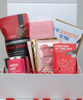 Gift box with various items including tea, cards, and candies on a heart-patterned surface.