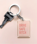 An acrylic keychain with a pink square tag that says 'DRIVE SAFE BITCH' attached to a key.