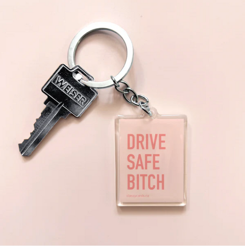 An acrylic keychain with a pink square tag that says 'DRIVE SAFE BITCH' attached to a key.
