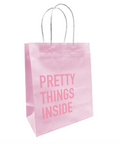 A pink paper gift bag with 'PRETTY THINGS INSIDE' printed in capital letters on the side, featuring twisted paper handles.