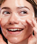 Woman applying a skincare product to her face with a purple background