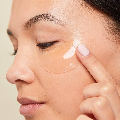 Person applying a patch to their eye with a neutral background