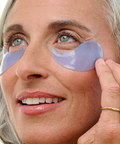 Woman applying purple eye patches to her eyes