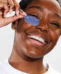 Person applying a blue eye mask to their eye with a hand