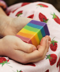 Child's hands holding a rainbow-colored block with a strawberry-patterned blanket in the background