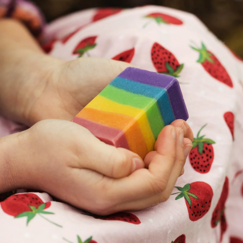 Child's hands holding a rainbow-colored block with a strawberry-patterned blanket in the background