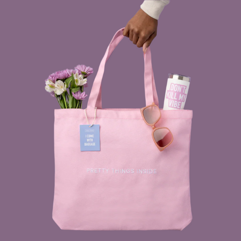 Pink tote bag with flowers, sunglasses, and a tumbler on a purple background