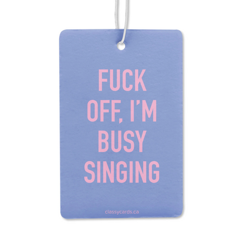 Blue air freshener with pink text 'FUCK OFF, I'M BUSY SINGING' on a white background