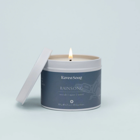 Candle in a tin with 'Raven Song' branding on a light gray background