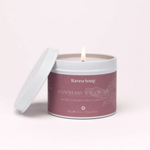 Candle in a tin labeled 'Raven Soap' with 'Wild Berries + Fireweed' on a light pink background