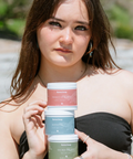 Woman holding three small containers outdoors with a blurred natural background