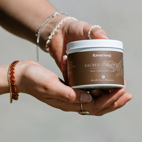 Person holding a container labeled 'RavenSong Sacred Tobacco' against a neutral background