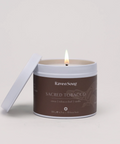 Candle in a brown container labeled 'Raven Song Sacred Tobacco' on a light gray background