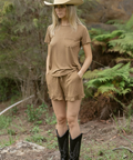 Person wearing a beige cowboy hat, brown shirt, and shorts standing in a natural setting.