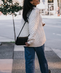 Woman wearing a white cable knit sweater and blue jeans walking on a city street.