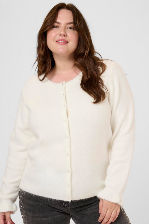 Woman wearing a white cardigan and dark jeans on a white background
