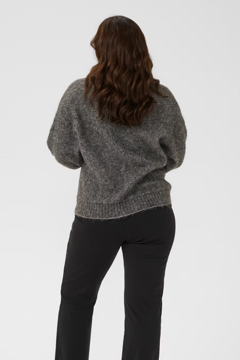 Person wearing a gray sweater and black pants on a white background