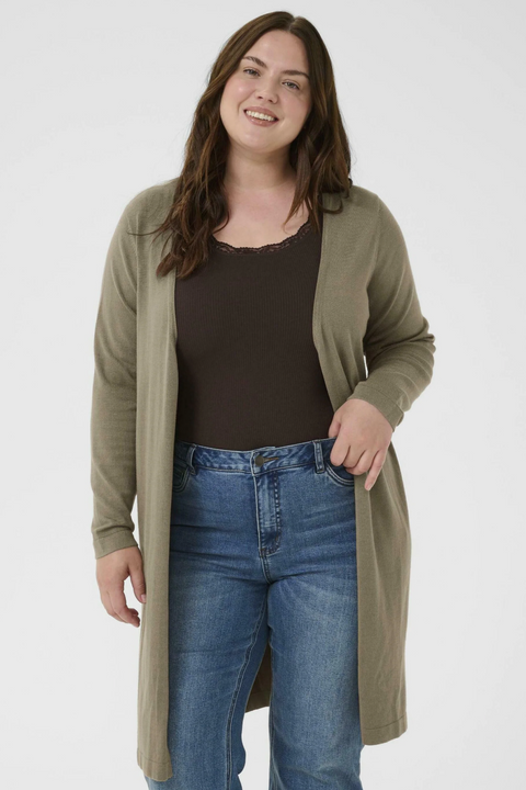 Woman wearing a long olive green cardigan, black top, and blue jeans on a white background