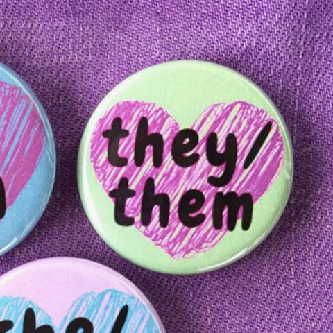 Three buttons with pronoun text on a purple fabric background