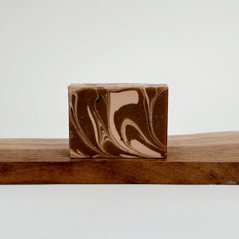 Marbled brown and beige soap bar on a wooden surface with a white background