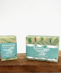 Two bars of 'Raven Song' soap with packaging on a wooden surface