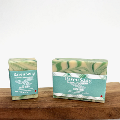 Two bars of 'Raven Song' soap with packaging on a wooden surface