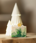 Green marbled soap with a gold star on a wooden surface, blurred Christmas tree in the background