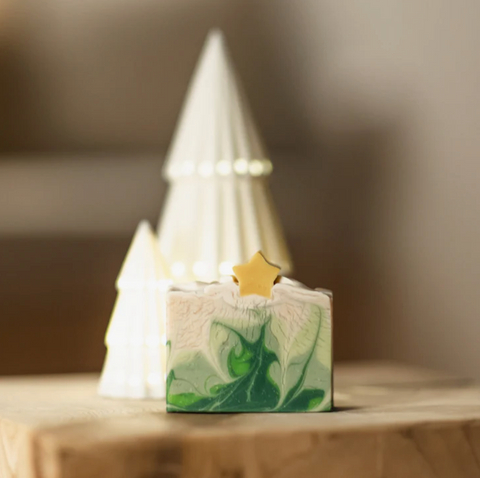 Green marbled soap with a gold star on a wooden surface, blurred Christmas tree in the background