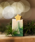 Decorative candle with a star on top, surrounded by greenery with a blurred light background