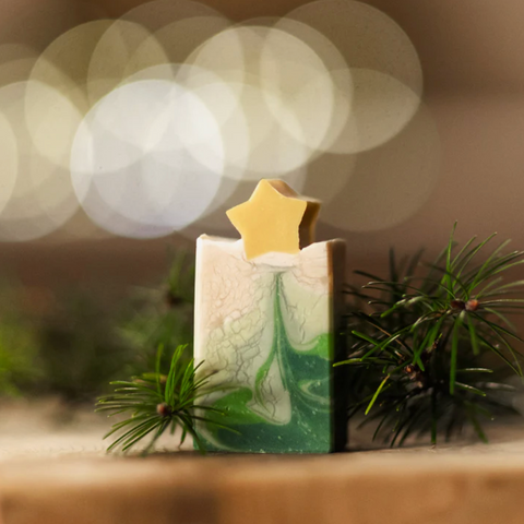 Decorative candle with a star on top, surrounded by greenery with a blurred light background