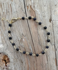 Black beaded bracelet on gold chain on a wooden surface
