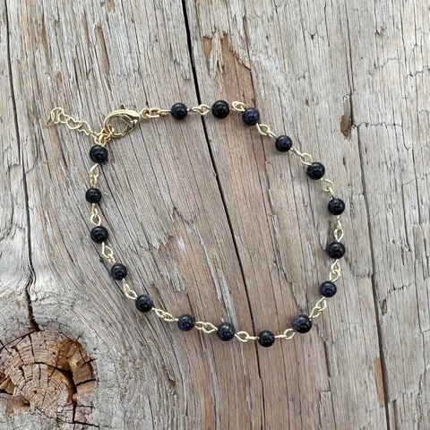 Black beaded bracelet on gold chain on a wooden surface