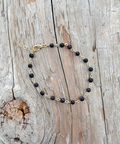 Necklace with black beads and gold chain on a wooden surface