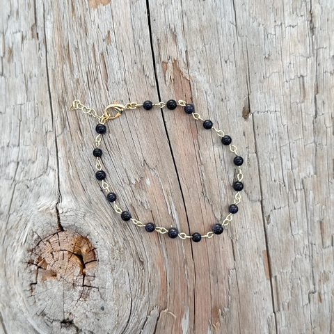 Necklace with black beads and gold chain on a wooden surface