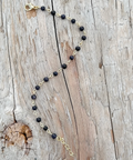 Necklace with black beads and gold chain on a wooden surface