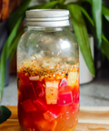 Glass jar with a metal lid on a wooden surface with plants in the background