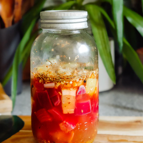 Glass jar with a metal lid on a wooden surface with plants in the background