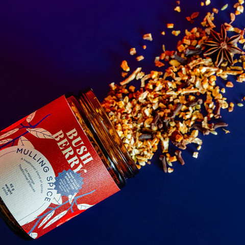 Mulling spice blend spilling out of a red and white container on a dark blue background