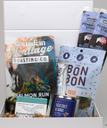 Assorted food items including a can of 'Canadian Heritage Roasting Co.' salmon run, 'Bon Bon' gummies, and 'Raven Song' tea in a box.