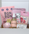 Gift box with various items including a pink bath bomb, gummies, and tea包