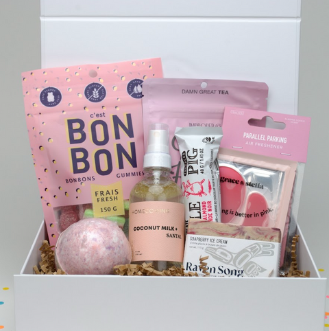 Gift box with various items including a pink bath bomb, gummies, and tea包