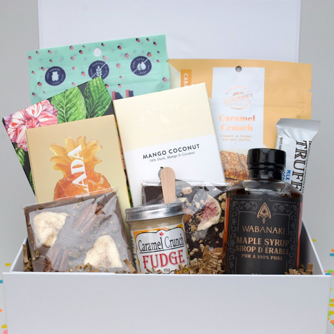 Assorted food items including a bottle of Wabanaki maple syrup, fudge, and other packaged goods in a box.