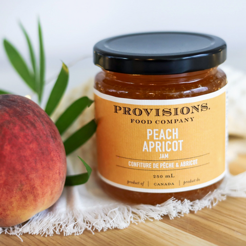 Jar of Provisions Food Company Peach Apricot Jam with a peach and leaves on a wooden surface.