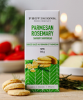 Box of Parmesan Rosemary shortbread cookies on a wooden surface with blurred food items in the background.