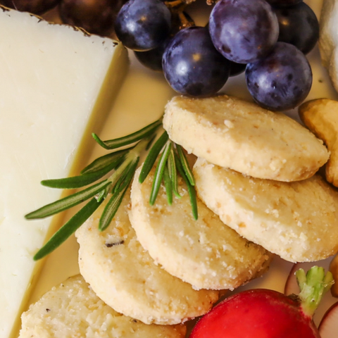 Platter with crackers, grapes, and a red pepper on a white surface
