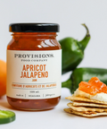 Jar of Provisions Apricot Jalapeno jam with apricots, jalapenos, and crackers on a white background